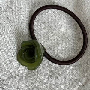Dettaglio dell'elastico per capelli con rosa in acetato verde su sfondo di lino