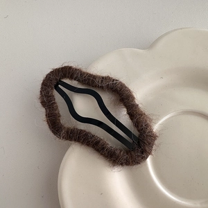 Close-up of a brown plush cloud hair clip with wave-shaped metal BB clip on a floral plate