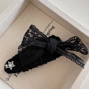 Detail van een zwarte kanten strik haarclip met zilveren ster op een textuur plateau