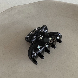 Dettaglio macro del mollettone in acetato nero con strass e scritta dorata artigianale