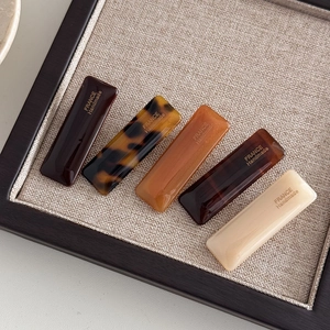 Detail showing five assorted rectangular acetate hair clips in elegant earth tones
