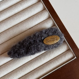 Gros plan d'une pince à cheveux en tricot gris foncé avec étiquette dorée faite à la main