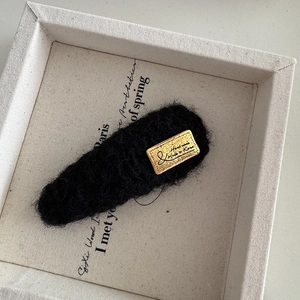 Détail d'une pince à cheveux ovale noire tricotée avec étiquette dorée faite main