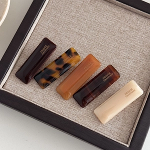 Close-up of five rectangular acetate hair clips in coffee tones with handmade logo