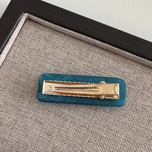 Detail view of the golden metal alligator clip and dark teal resin hair clip