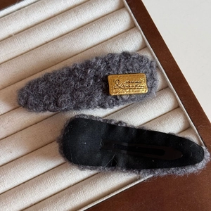 Détail de pinces à cheveux en tricot gris avec étiquette dorée et structure en métal noir