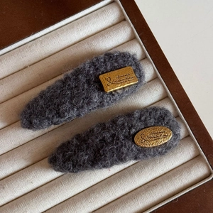 Détail de barrettes en peluche grise avec des étiquettes dorées gravées fait main