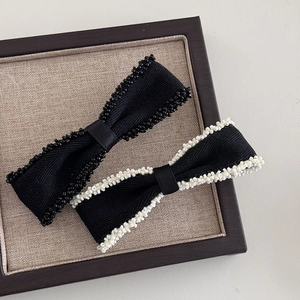 Elegant bow hair clips with beaded edges in black and white fabric on a tray