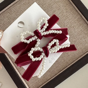 Macro detail of two handmade burgundy velvet bow hair clips with embedded white pearls