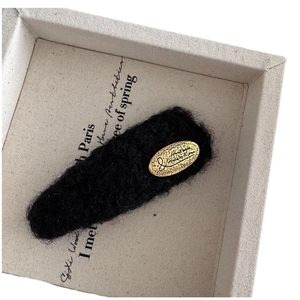 Barrette en tricot noir avec étiquette dorée ovale sur boîte de présentation beige