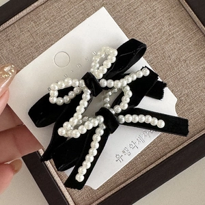 Close-up of black velvet bow hair clips with white pearl trim on elegant card