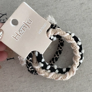 Dettaglio di elastici intrecciati nero e beige con piccoli pompon di peluche