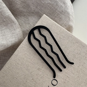 Détail d'épingle à cheveux ondulée à 4 dents noir mat sur un fond crème texturé