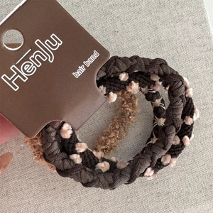 Primo piano di elastici per capelli intrecciati marroni con pompon su scheda di marca