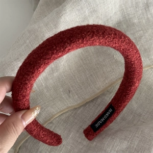 Detail of dark red textured wool headband with a handmade label on beige linen background