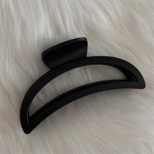 Détail d'une pince à cheveux noir mat en forme de croissant sur un tissu blanc doux
