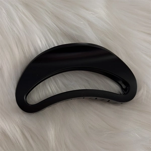 Gros plan d'une pince à cheveux noire mate évidée montrant la texture sur peluche blanche