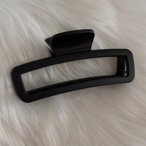 Gros plan d'une pince à cheveux rectangulaire noir mat sur fond en peluche blanche