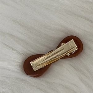 Macro detail of brown bow hair clip showing the durable gold metal duckbill clip back