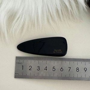 Fermaglio per capelli a goccia in acetato nero con logo dorato su sfondo in pelliccia
