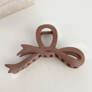 Close-up of matte brown bow hair claw clip showing elegant frosted texture on beige background