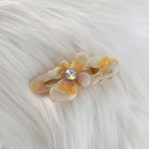 Close-up of small floral acetate hair clip with rhinestones on white faux fur background