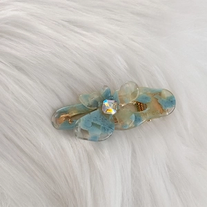 Detail of blue acetate flower hair clip with crystal center on white plush background