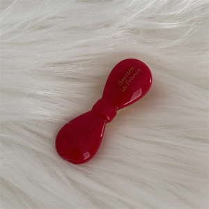 Detail of red acetate bow hair clip with gold logo on soft white faux fur background