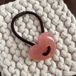 Vista macro di un elastico per capelli con cuore in resina rosa su tessuto a maglia bianco