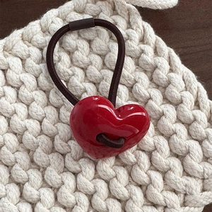 Dettaglio di un elastico per capelli a cuore rosso lucido su sfondo in tessuto beige