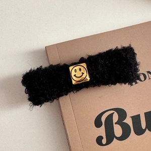 Close-up of a black curly faux shearling hair clip with a golden square smiley metal buckle