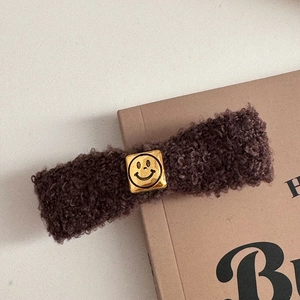 Detailed view of plush coffee brown faux fur hair clip with golden smiley face plate