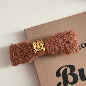 Detail shot of brown teddy fur bow hair clip with a golden smiley face metal buckle