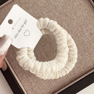 Detailed view of two plush cream hair scrunchies with white retail paper card packaging