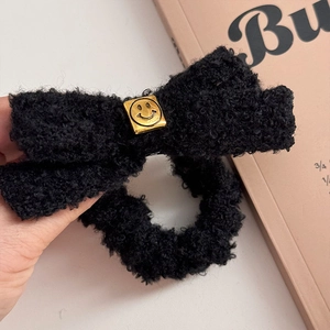 Close-up of black plush bow hair tie with a golden smiley face metal buckle detail