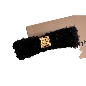 Plush black lamb wool hair clip featuring a square golden smiley face metal emblem