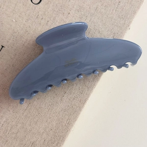 Détail d'une élégante pince à cheveux bleue en résine avec texte doré sur fond de lin