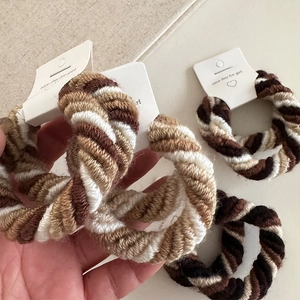 Detail of multi-strand braided hair scrunchies in coffee and cream tones with labels