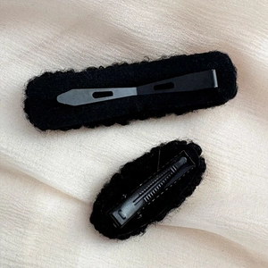Detail of two black plush faux fur hair clips with gold buttons on beige fabric