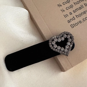 Close-up of black velvet hair clip with sparkling rhinestone heart on white fabric