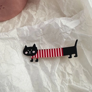 Detail view of a long black cat brooch with red and white stripes on textured paper