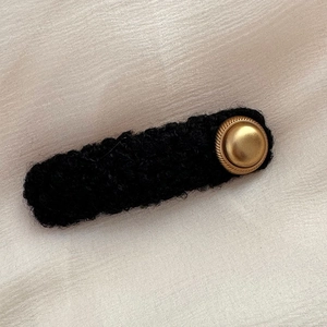 Close-up of black knitted hair clip with vintage golden button detail on textured fabric