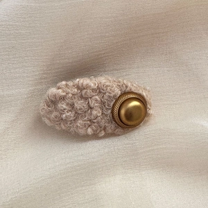 Detailed close-up of beige faux shearling hair clip featuring a vintage gold button