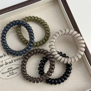Five assorted elastic spiral hair ties in olive, blue, and brown tones on a wooden tray