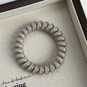 Close-up of translucent grey spiral hair tie on a decorative beige textured tray