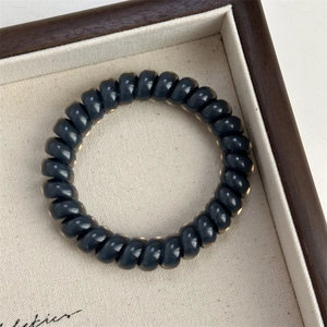 Macro view of dark grey spiral hair tie showing smooth glossy resin texture in a box