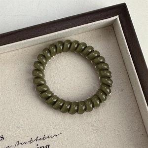 Detail view of glossy olive green spiral hair tie displayed in a wooden jewelry box