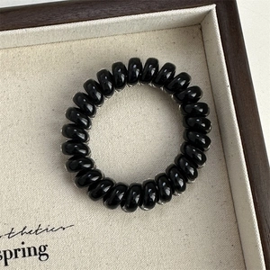 Macro shot of a glossy black spiral telephone wire hair tie on a minimalist wooden tray