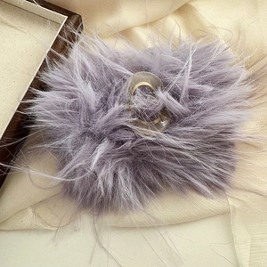 Dettaglio della pinza per capelli in peluche viola chiaro con molla dorata e piume soffici