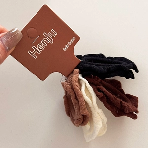 Close-up of set of 4 ruffled fabric hair bands in black, brown, and beige on card